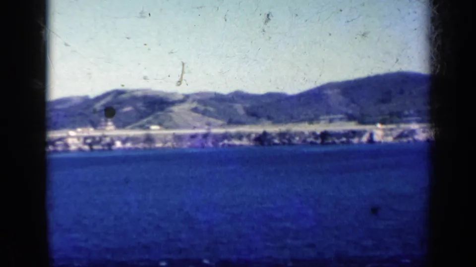Soft 8mm frame of a Cuban shoreline and hills across deep blue water, with dust and slight blur from the pan.