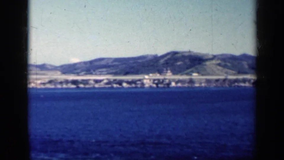 1962 Cuba home-movie frame looking over blue water to a low shoreline and hills, with visible 8mm borders.