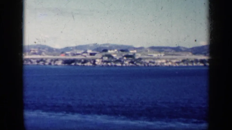 1962 Cuba 8mm frame showing the moving coastal view across blue water, with low buildings and hills on the horizon.