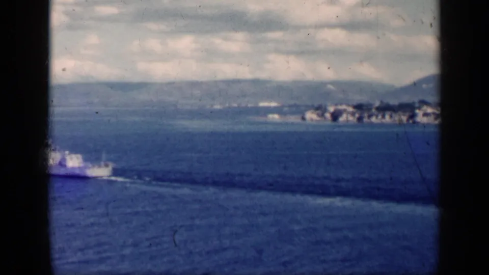 1962 Cuba 8mm view with a ship at lower left crossing blue water before a distant shoreline and hills.