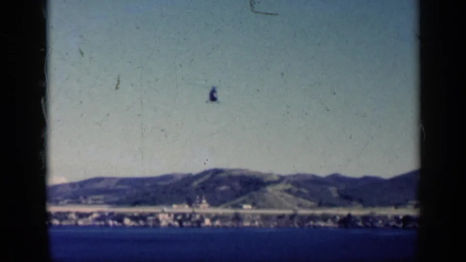 1962 Cuba 8mm frame of blue water, distant coast, green hills, and a helicopter passing above the horizon.