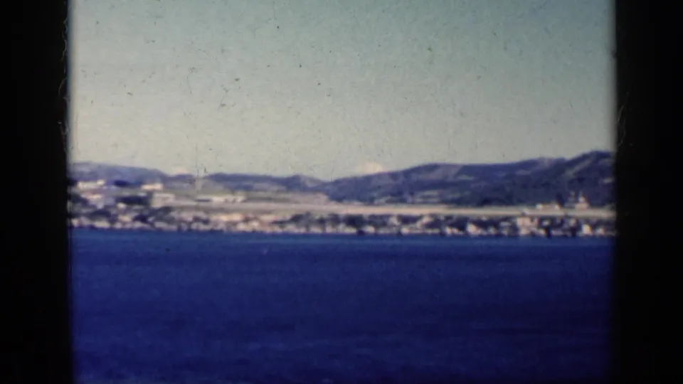 1962 Cuba travel footage frame with open blue water, distant coastal development, and hills across the horizon.