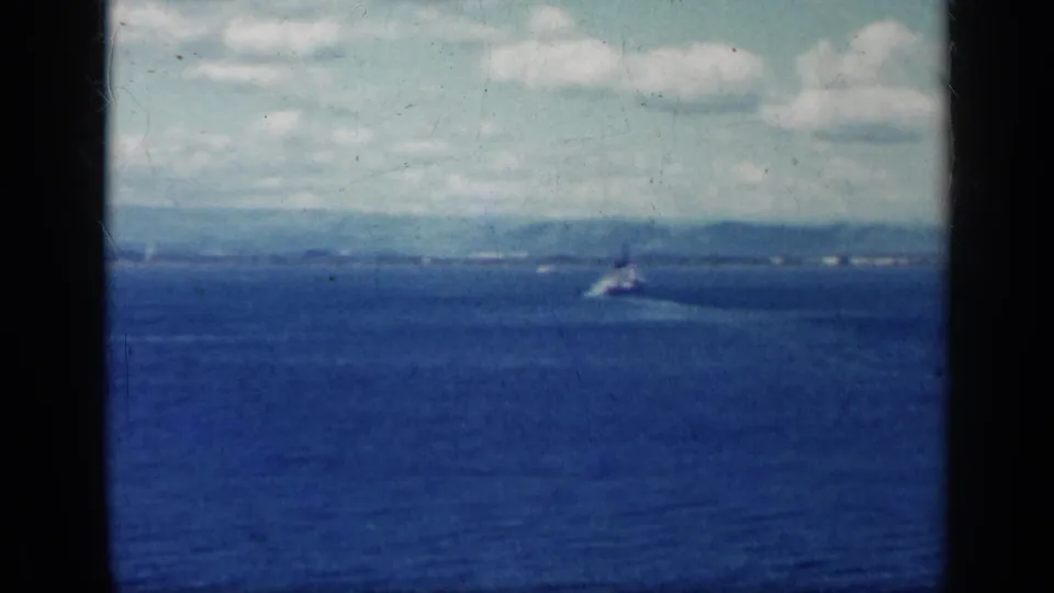 1962 Cuba coastal frame showing a small boat crossing blue water in front of a distant shoreline and clouded sky.
