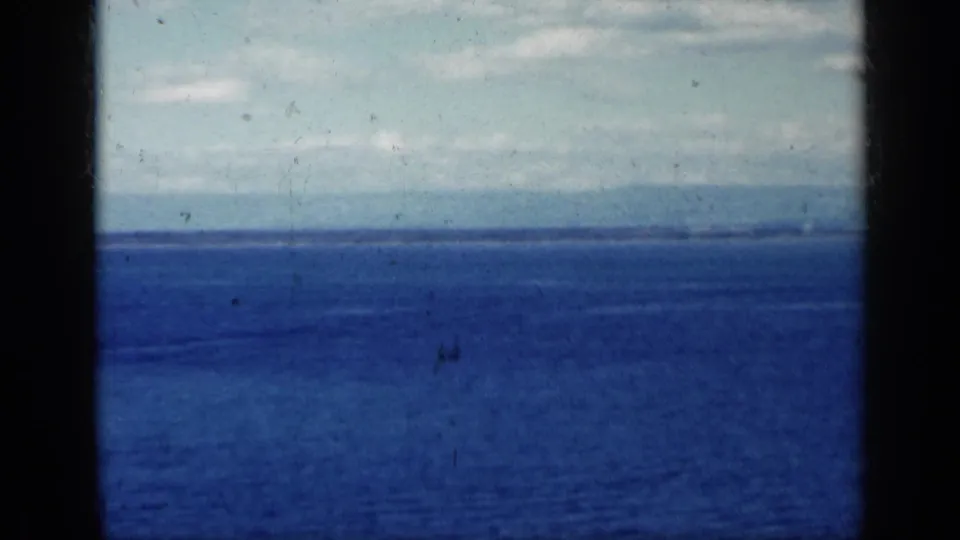 1962 8mm footage shows open water and a far shoreline, with a small distant boat or wake near the horizon.