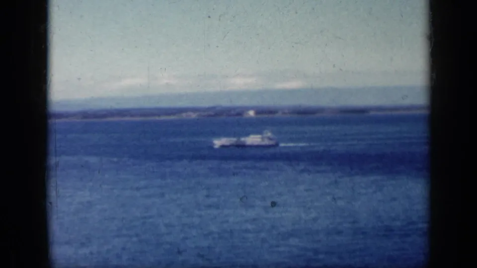 1962 Cuba coastal water view with a small boat crossing beneath a pale sky, framed by dark aircraft-window edges.