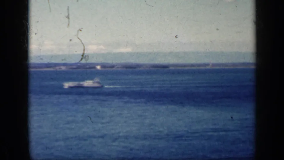 1962 Cuba aerial coastal frame with a boat on the water, low shoreline in the distance, and visible 8mm film wear.