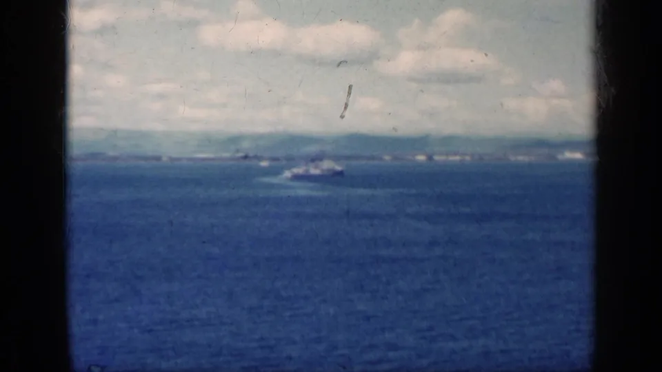 Wide 8mm view from Cuba in 1962 with a distant vessel on blue water and a hazy coastline beyond.