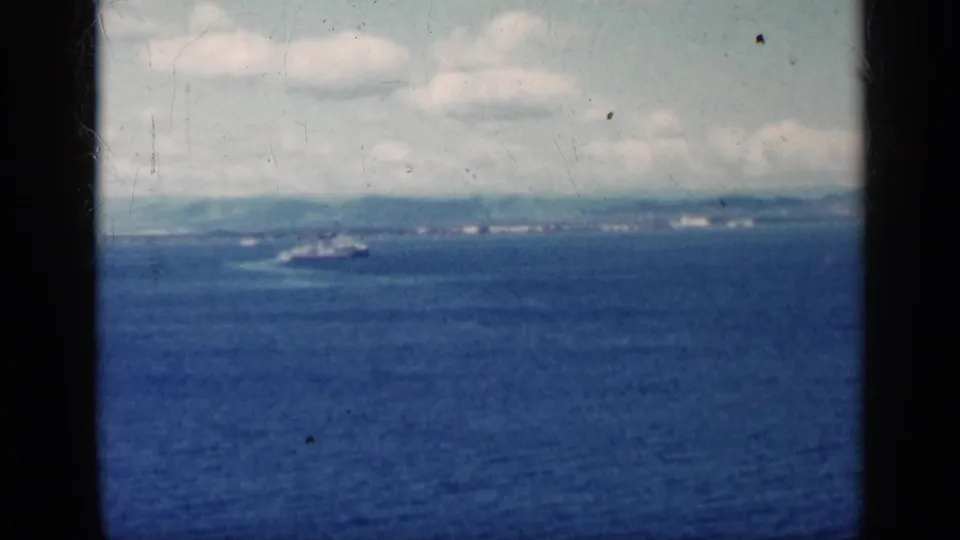 Final 1962 Cuba home-movie frame showing a small boat offshore beneath scattered clouds with visible 8mm film texture.