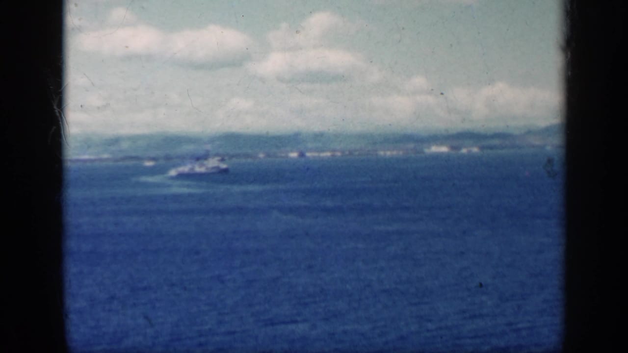 Blue ocean with a distant ship, low coastline, clouds, and dark film borders.