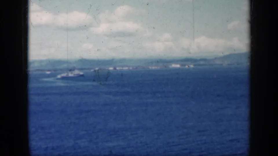 1962 Cuba coastal view with open blue water, a small ship near the horizon, faint shore structures, and bright cloud cover.