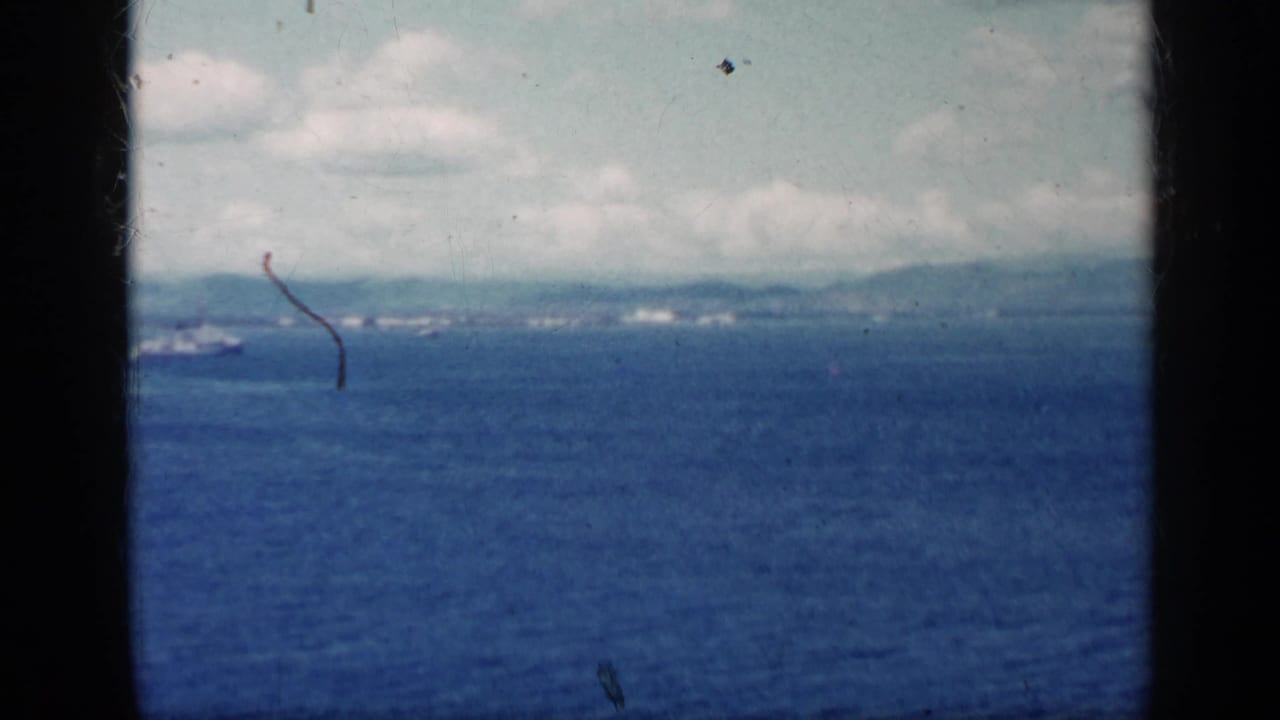 Blue ocean seen through dark film frame edges with distant land and ships on the horizon.