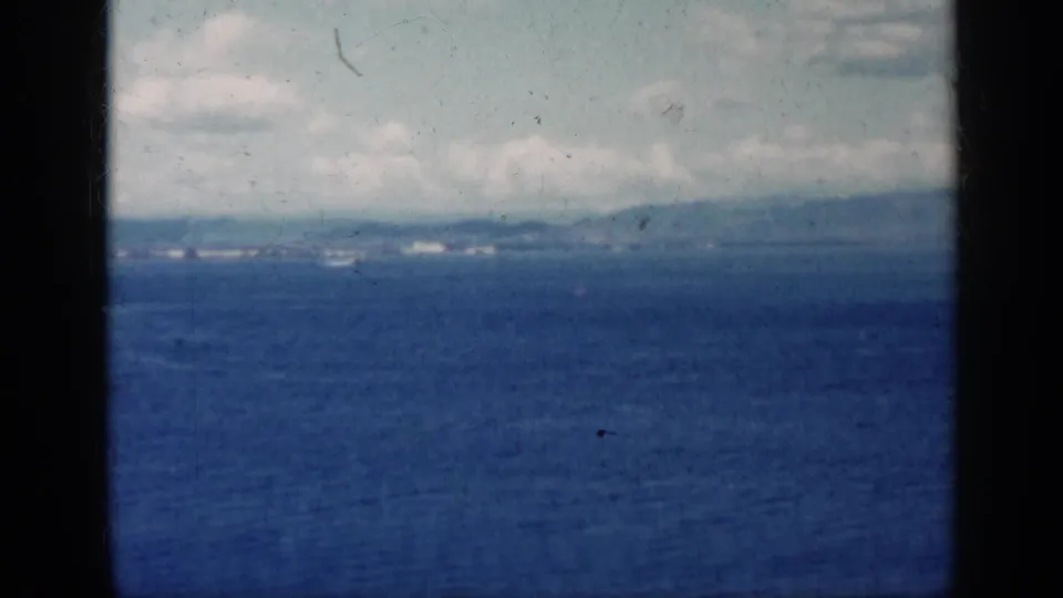 Cuba-linked 1962 8mm view of blue sea, hazy land on the horizon, pale clouds, and heavy vertical frame borders.
