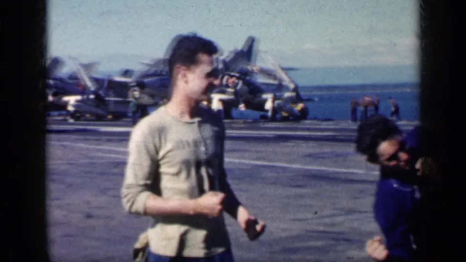 Cuba-associated 1962 8mm frame of a man in a light sweater facing a man in blue on a naval carrier deck.