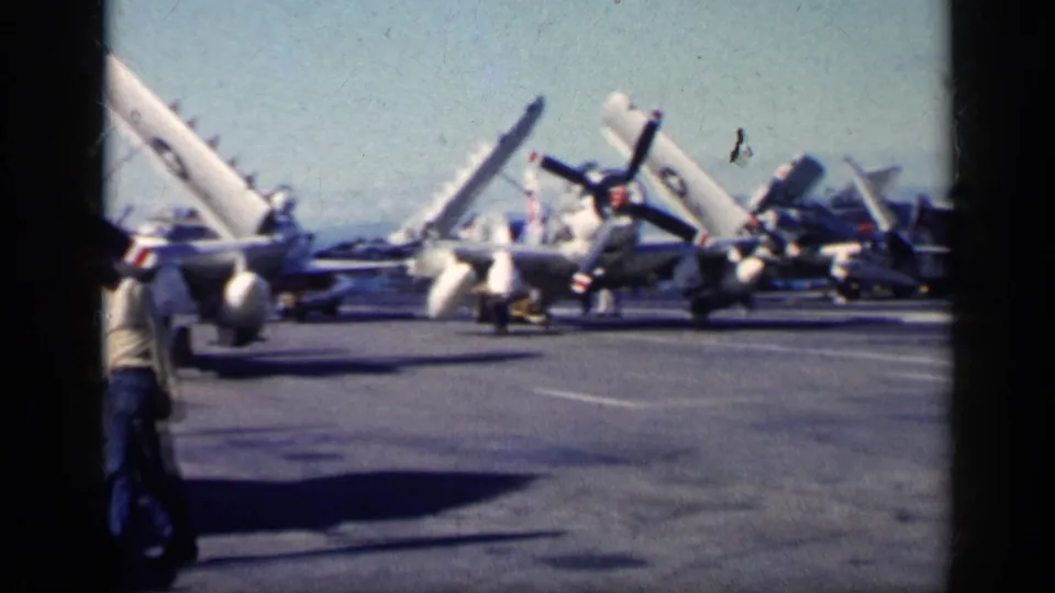 Cuba-associated 1962 8mm frame of naval aircraft parked on a carrier deck with a walking figure in the foreground.