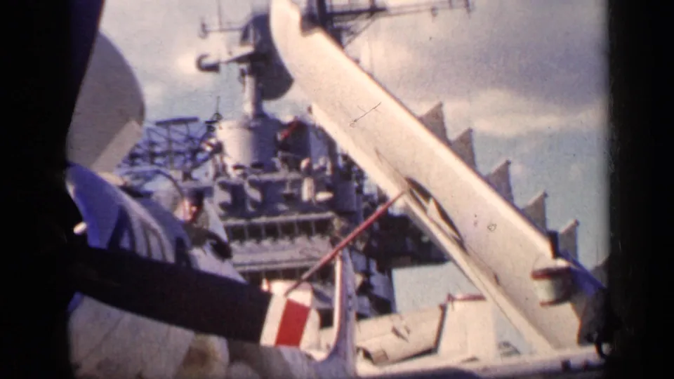A carrier deck view from the Cuba 1962 footage shows a raised aircraft wing, aircraft tail, and ship superstructure in the background.
