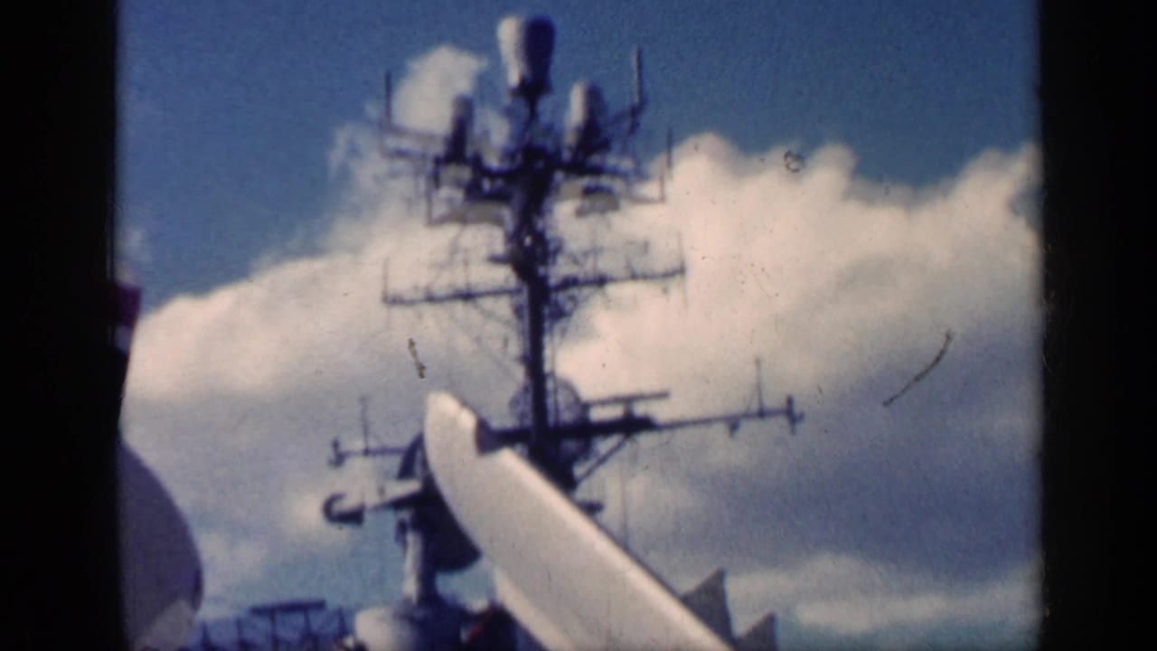 Aircraft carrier mast and radar structures against clouds, seen from the deck.