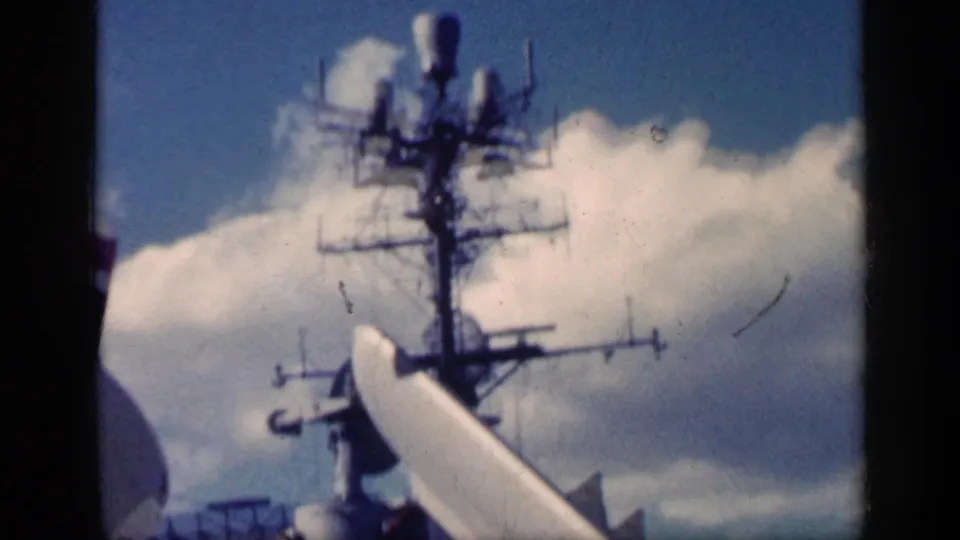 1962 8mm frame showing an aircraft carrier mast and deck structures under a cloudy sky near Cuba, per clip metadata.
