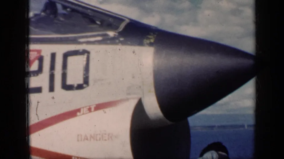 Military jet nose and cockpit with number 210 and red safety markings, shown on a carrier deck in the 1962 Cuba clip context.