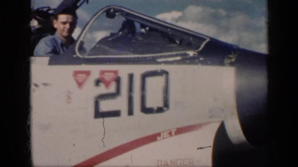 A pilot sits in an open cockpit beside the marked fuselage number 210, matching the 1962 U.S. naval aviation context in the metadata.