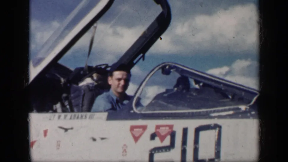 A young man sits in the open cockpit of a military jet in Cuba in 1962, with the painted number 210 partly visible below him.
