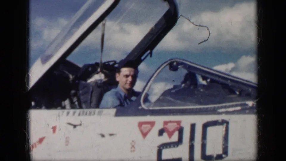 The 1962 Cuba footage shows the man in a blue shirt seated inside the jet cockpit, with canopy glass, fuselage markings, and sky behind him.