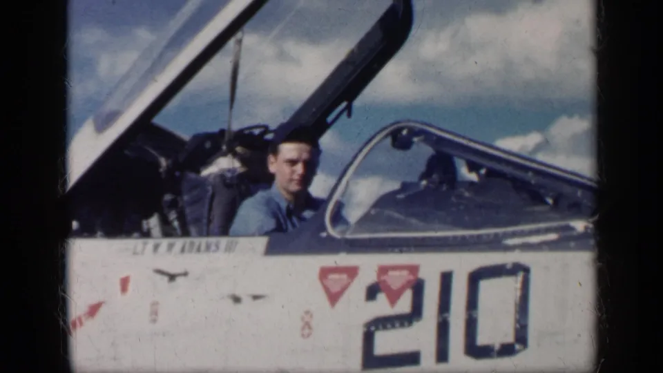 A young man looks toward the camera from the open cockpit of a military jet in Cuba in 1962, with number 210 visible on the fuselage.
