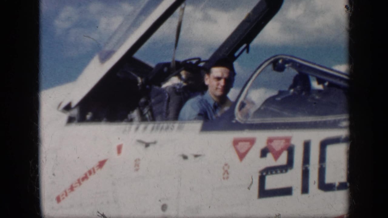 Pilot seated in an open jet cockpit beside the number 210 on the fuselage.