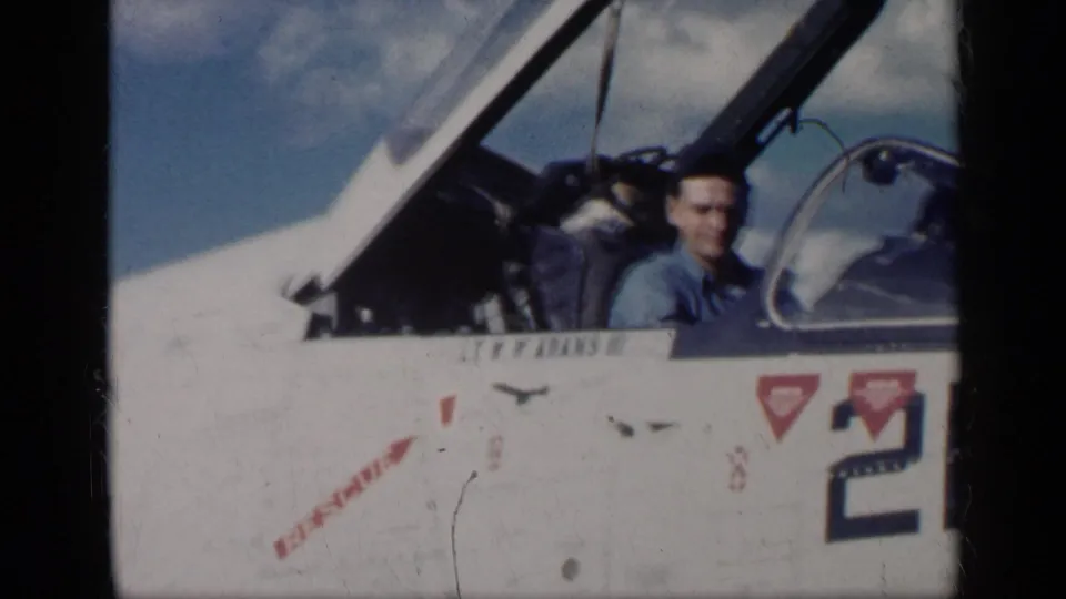 Pilot sits in the raised-canopy cockpit of a U.S.-marked military jet, with stenciling and partial aircraft number visible.