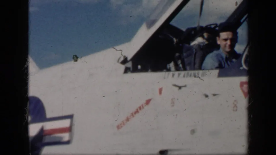 Cuba-associated 1962 home-movie frame showing the pilot above a white U.S.-marked jet fuselage with the star insignia partly visible.