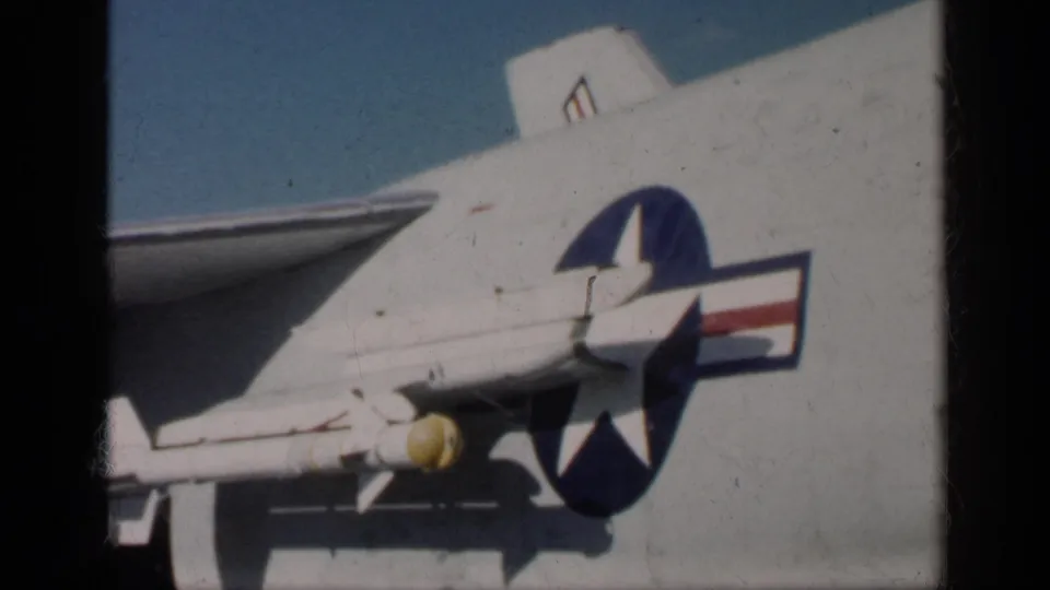 Close 8mm view of the aircraft fuselage and wing, with the U.S. star-and-bar insignia and yellow-tipped underwing object visible.