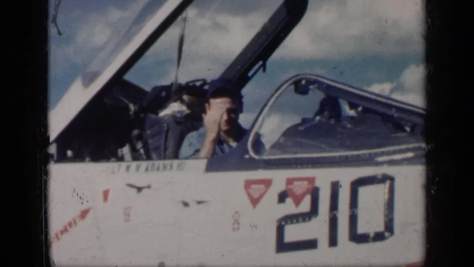 A man in a blue shirt and cap raises a hand from the open cockpit of a white jet in Cuba, 1962 per metadata.