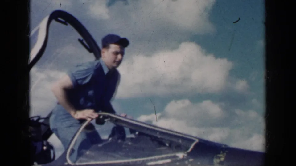 The man in blue clothing and cap begins climbing out of the open cockpit of the white military jet in Cuba, 1962 per metadata.