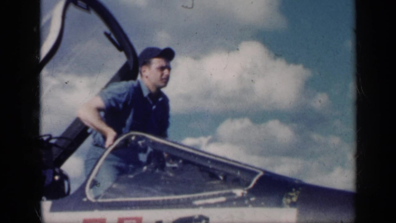Man in a cap climbs from an open aircraft cockpit under a cloudy blue sky.