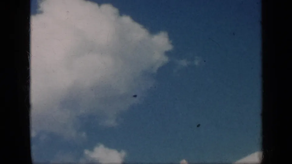 The final frame holds on open blue sky and scattered white clouds, with dust and gate edges from the 8mm scan visible.