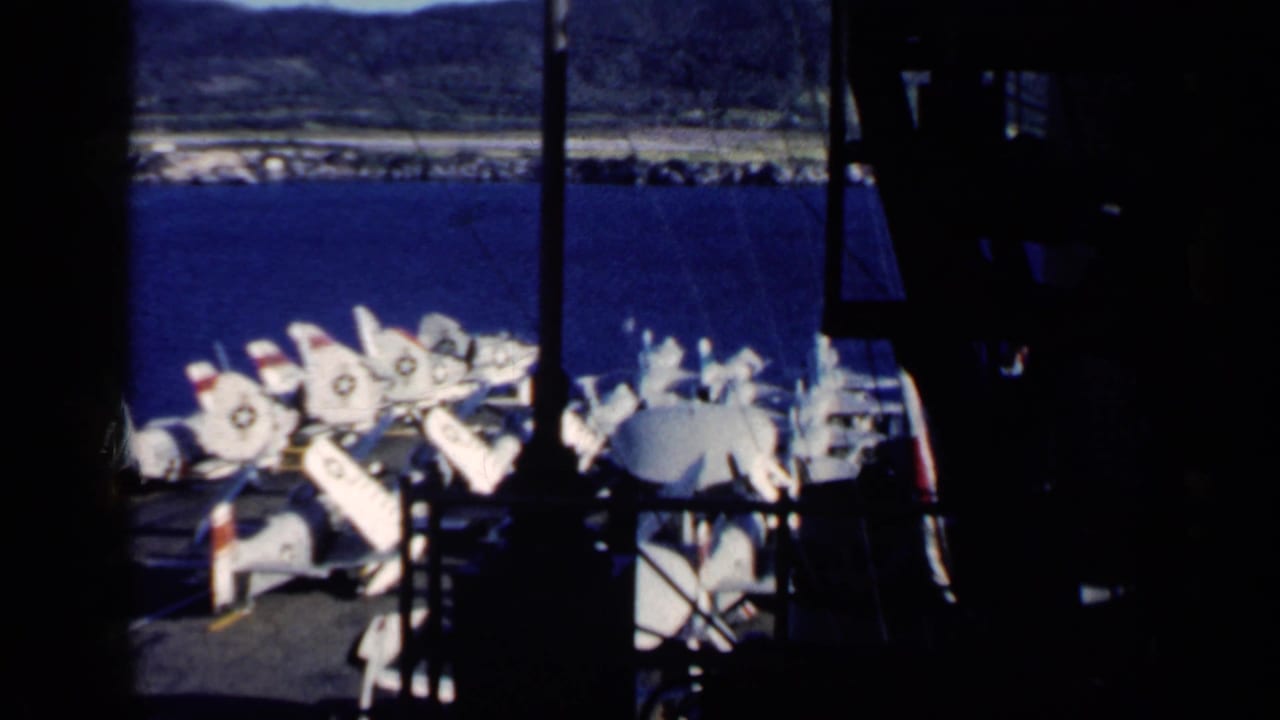 White Navy jets with folded wings parked on an aircraft carrier deck beside blue water.