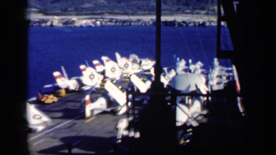 1962 Cuba-labeled carrier-deck view with rows of white Navy aircraft, folded wings, ship framing, and the coastline beyond the water.
