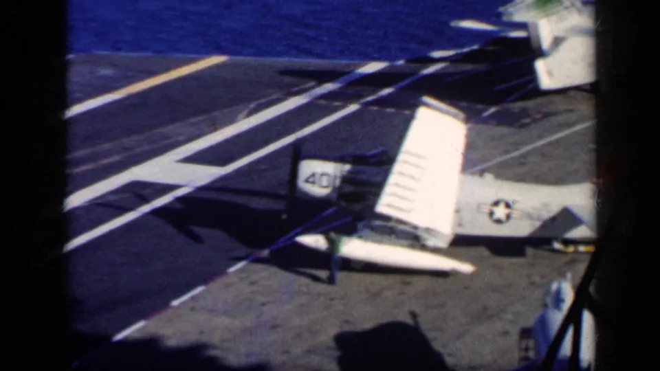1962 Cuba 8mm frame with a white U.S. Navy aircraft tail, wing, deck striping, shadows, and a partial crew figure.