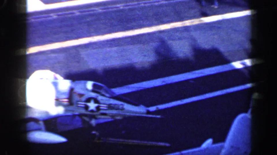 1962 catalog frame near Cuba showing a fighter jet on a U.S. carrier deck, with star insignia, deck lines, and film-frame obstruction.