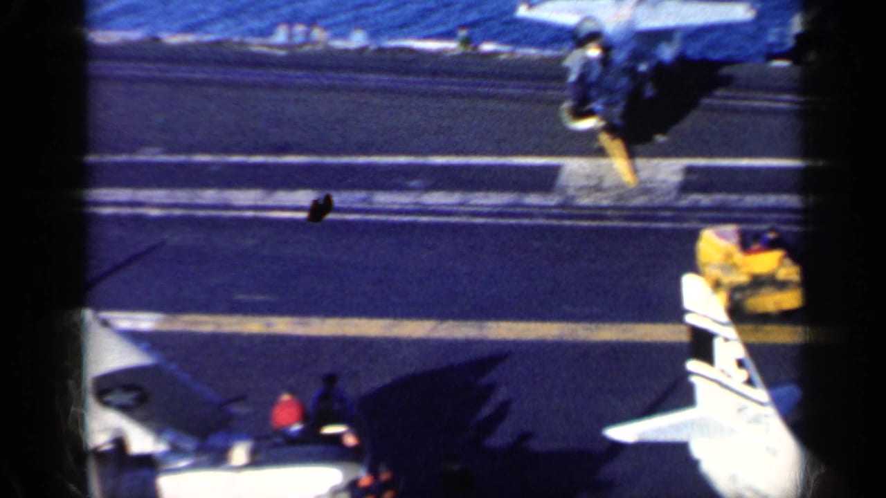 U.S. Navy aircraft parked on a carrier deck with ocean visible beyond the flight deck.