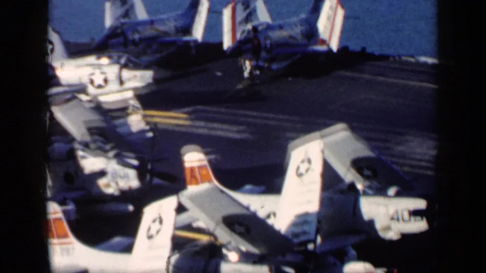 1962 8mm view of clustered U.S. Navy aircraft on a carrier deck near Cuba, with tail numbers and deck crew activity visible.