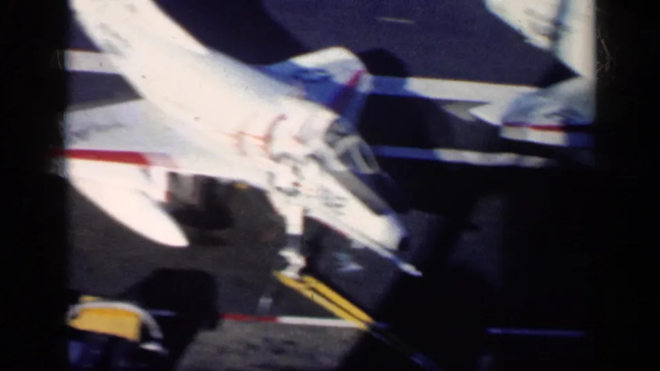 1962 8mm frame from supplied Cuba metadata showing a white military jet on a tarmac with markings, shadows, and yellow ground equipment.