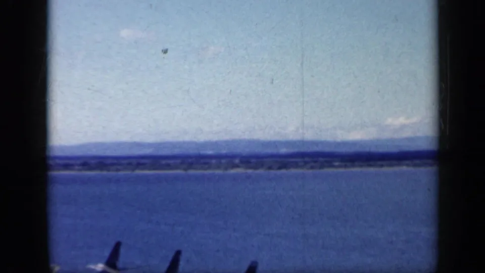 Grainy 8mm view of open water with a low distant coastline, matching the supplied Cuba 1962 clip context.