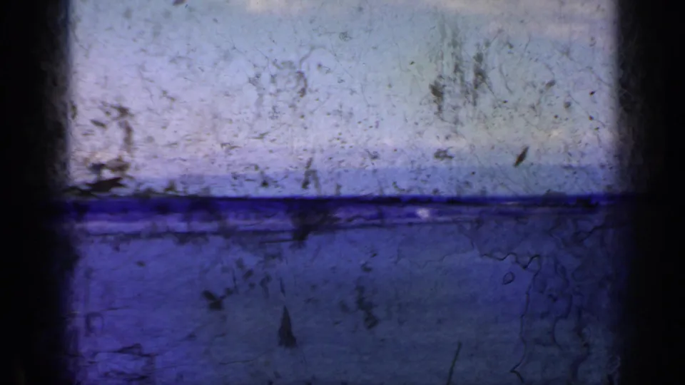 Blue-shifted 8mm frame of water and horizon, heavily marked by scratches, dirt, and age-related film texture.
