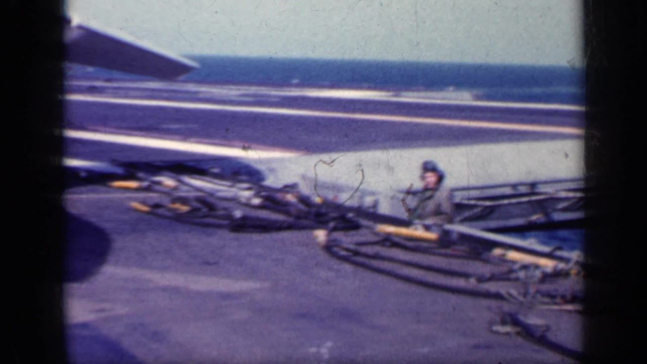 Sailor in helmet works near cables on an aircraft carrier deck at sea.