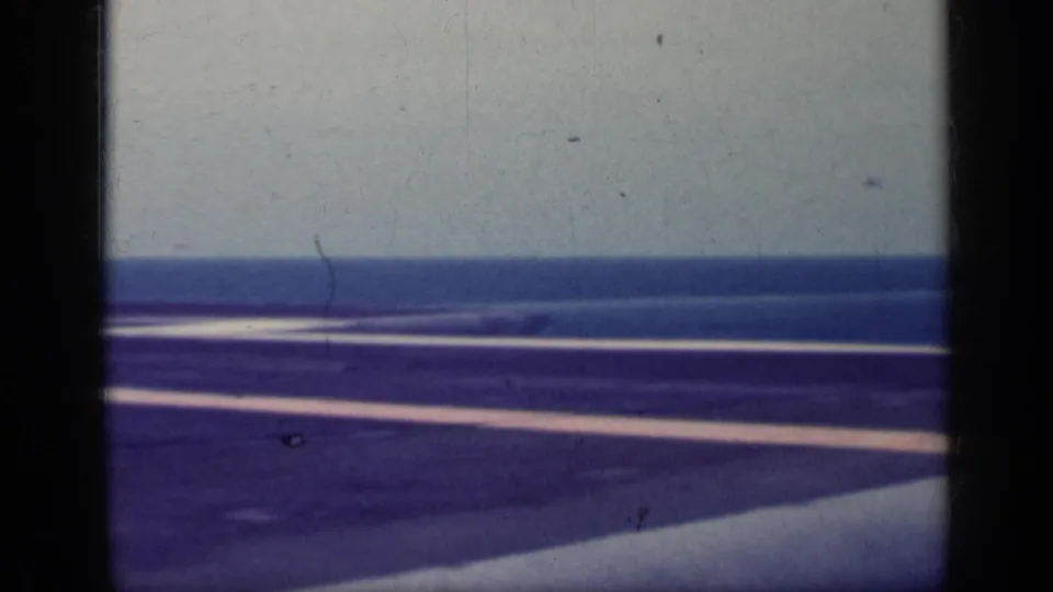 1962 Cuba-associated 8mm frame showing a carrier flight deck, white deck markings, ocean horizon, and dark foreground ship structure.