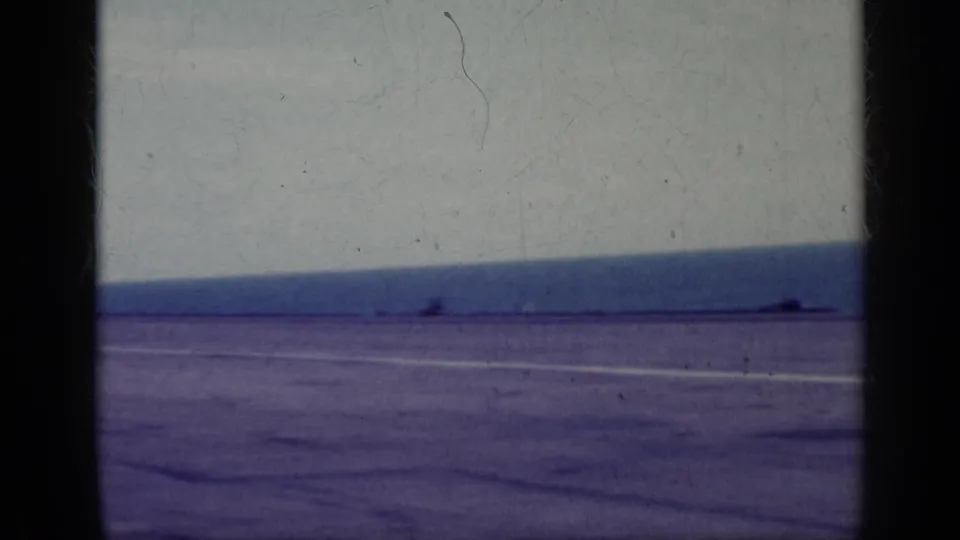 1962 Cuba 8mm frame showing a broad paved airfield near open water under a pale sky, with dark film borders.