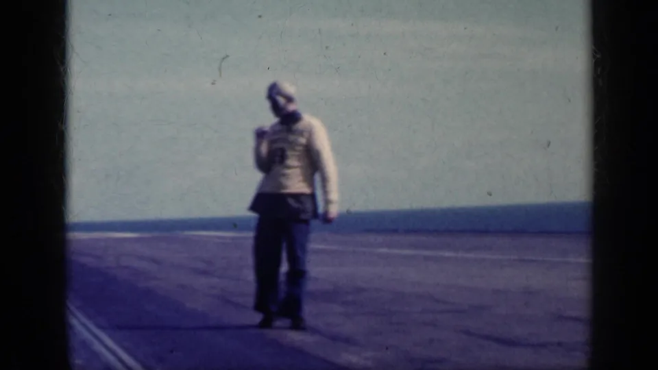 Adult man on a broad Cuba airfield in 1962, walking across the tarmac with the ocean horizon behind him.