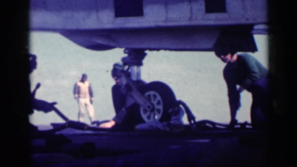 A wider 8mm view shows personnel gathered around aircraft landing gear on a carrier deck during the 1962 Cuba reel.