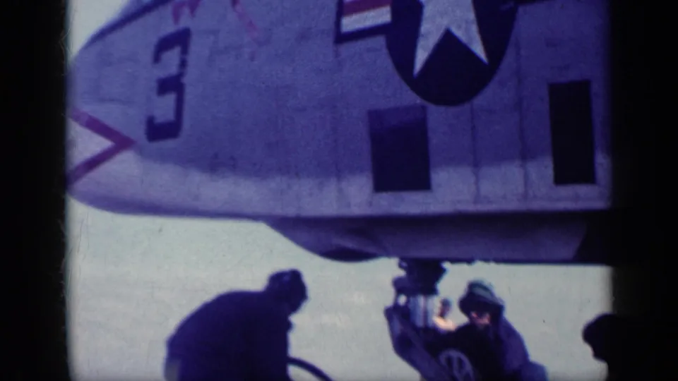 U.S. Navy aircraft fuselage markings, including a number 3 and star insignia, appear above crew working by the landing gear.