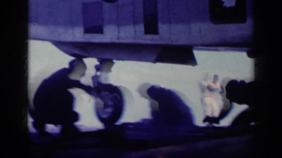 Uniformed crew appear in silhouette beneath a U.S. Navy aircraft, with landing gear and underside details visible on the carrier deck.